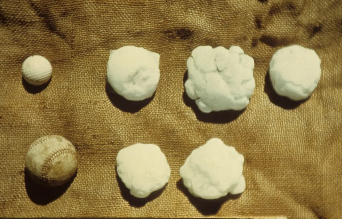 Six lumpy white baseball-size hailstones on burlap, next to a real baseball and a golf ball for scale