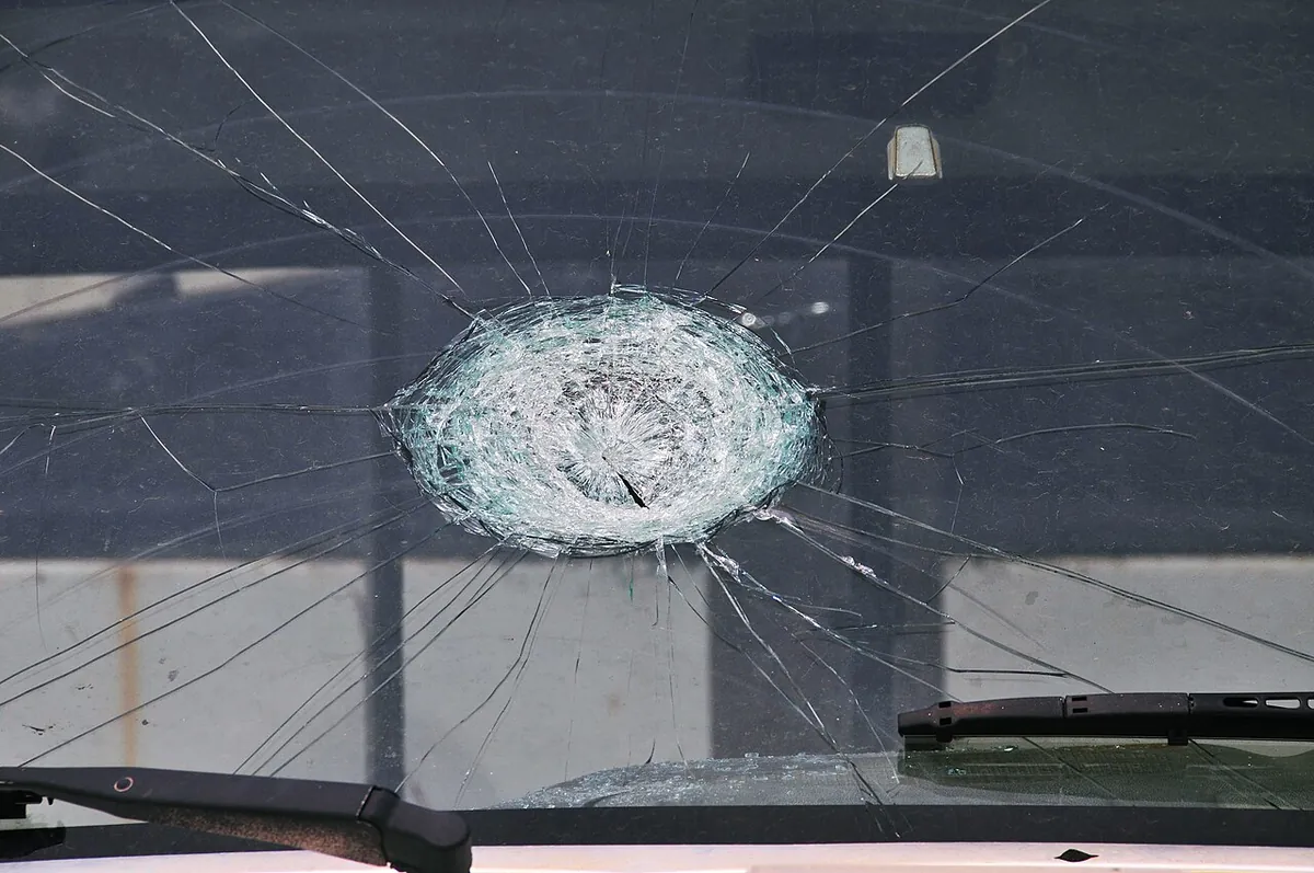 A car windshield shattered in a round spiderweb pattern where one large hailstone struck it